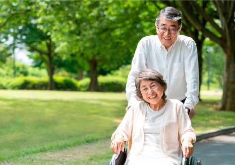 高齢の妻の車いすを夫が笑顔で押している画像